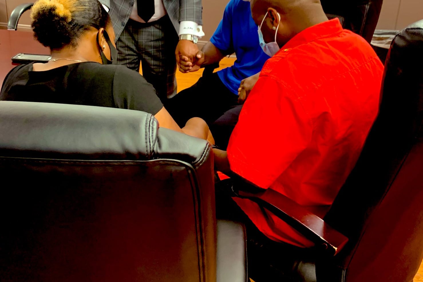 Four adults circled together in a conference room hold hands and pray.