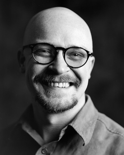 Black and white headshot of a bald man with a beard and glasses.