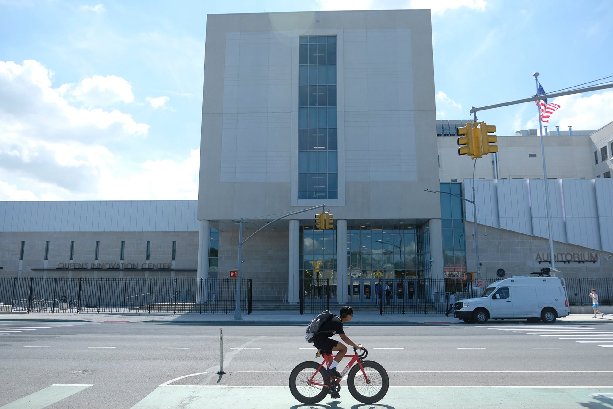 A photograph of a person riding their bike in front of a large school building.