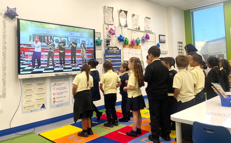 Students in uniforms stand in front of a screen.