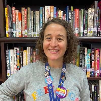 A woman with short hair poses with a smile in front of a bookshelf.