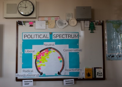 A colorful poster with the headline reading "Political Spectrum," hangs on a wall in a classroom.