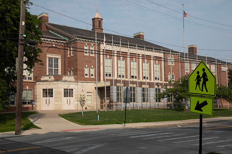 The front of a large stone school building with a crossing sign in the front.