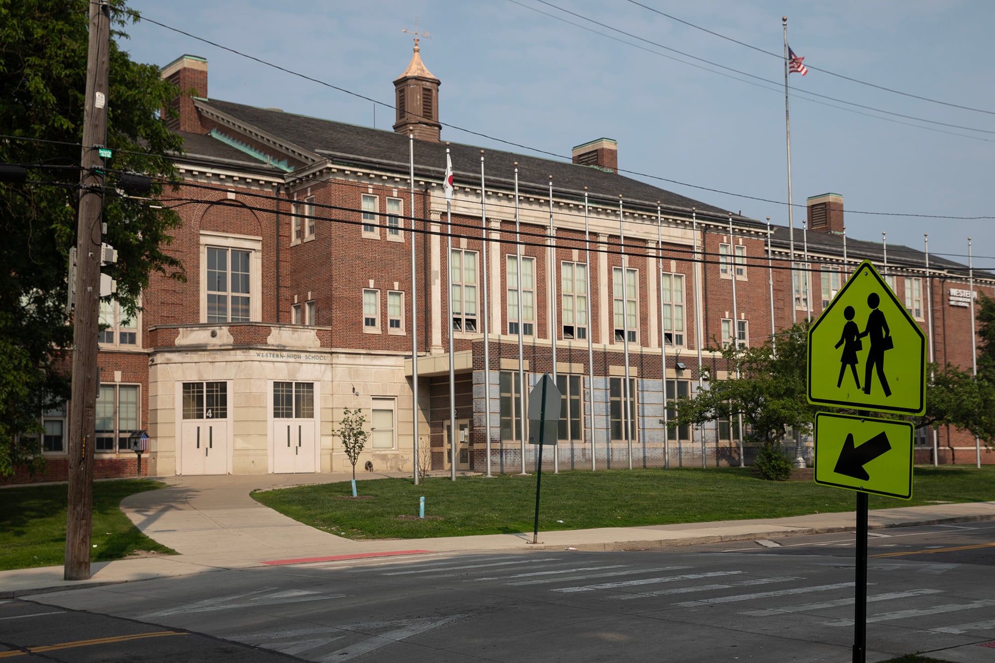 The front of a large stone school building with a crossing sign in the front.