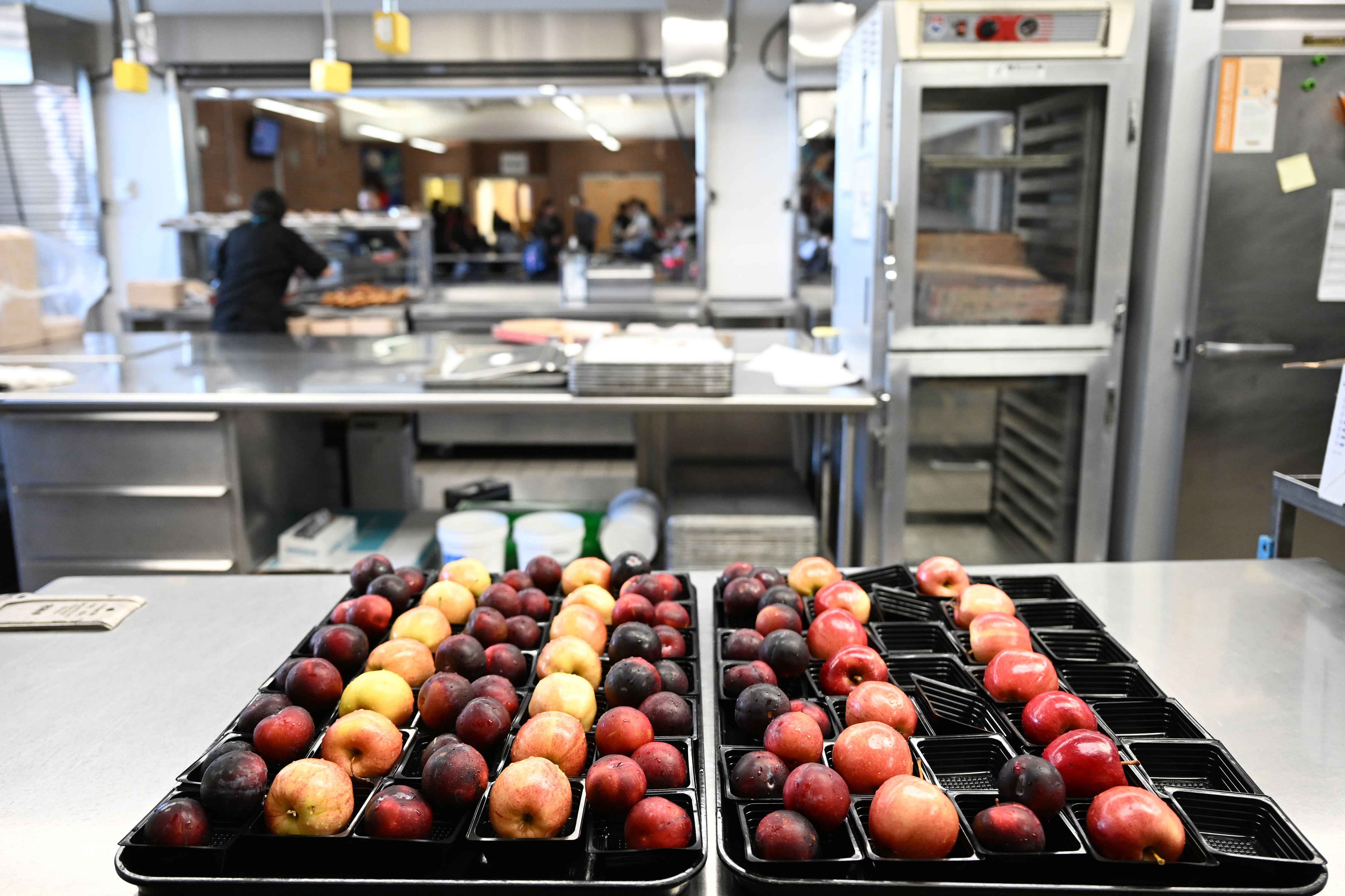 A tray of fruit sit on a school cafeteria in the foreground.