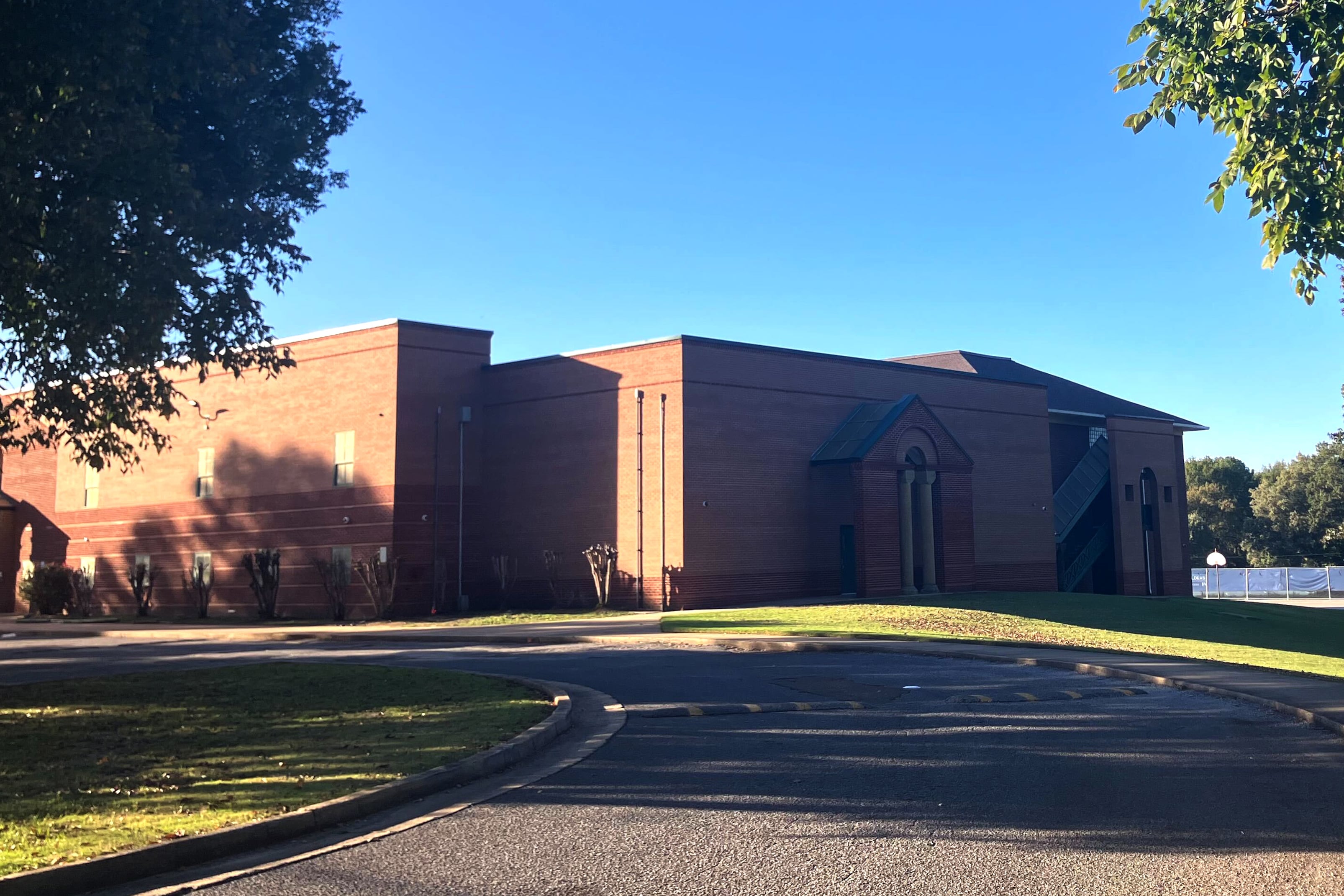 A photograph of a large brick school building with a clear blue sky in the background and green trees in the foreground.