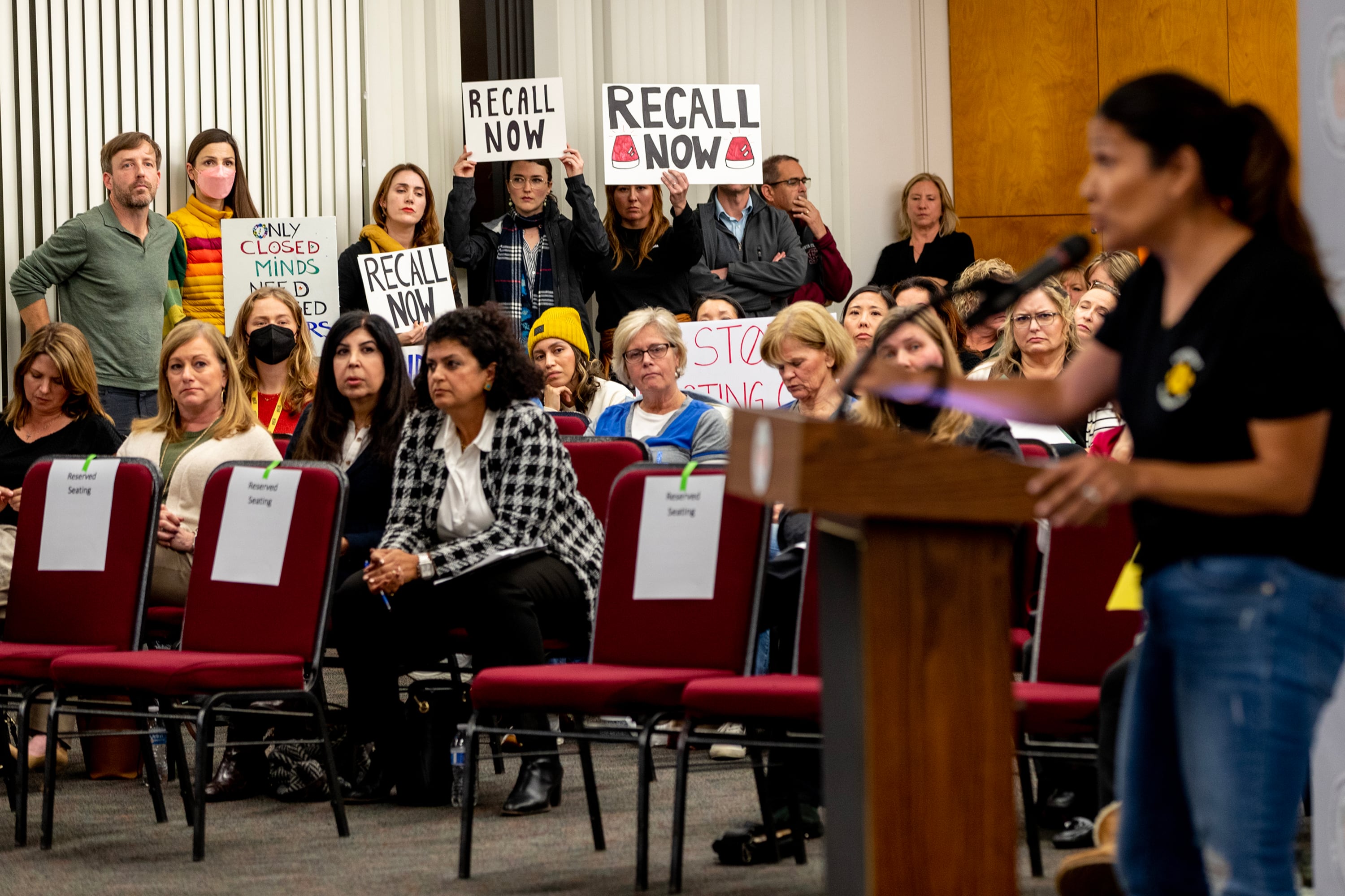 A crowd is in the background of a woman standing at a wooden podium.