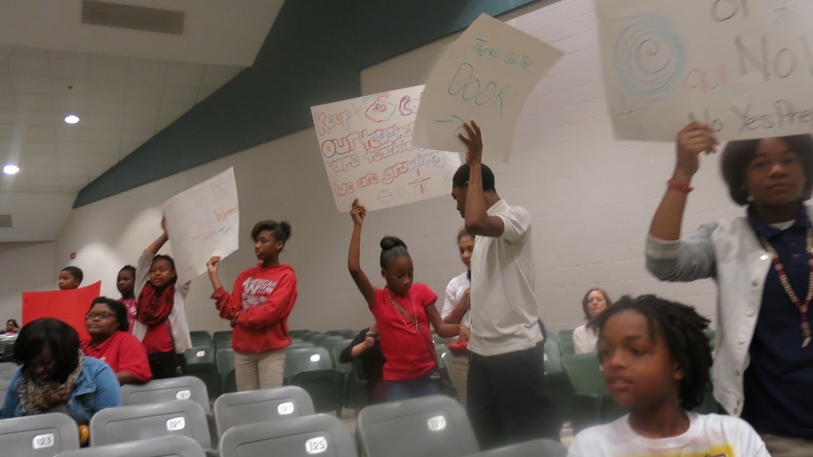 Several American Way students held signs during Monday night's school takeover community meeting with Yes Prep.