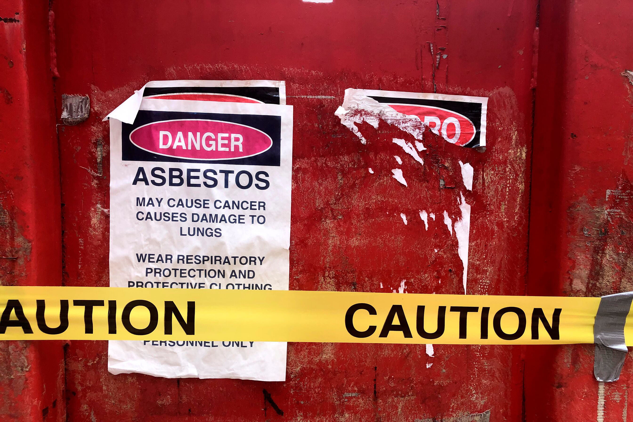 A bright red asbestos removal dumpster with caution tape and a warning sign.
