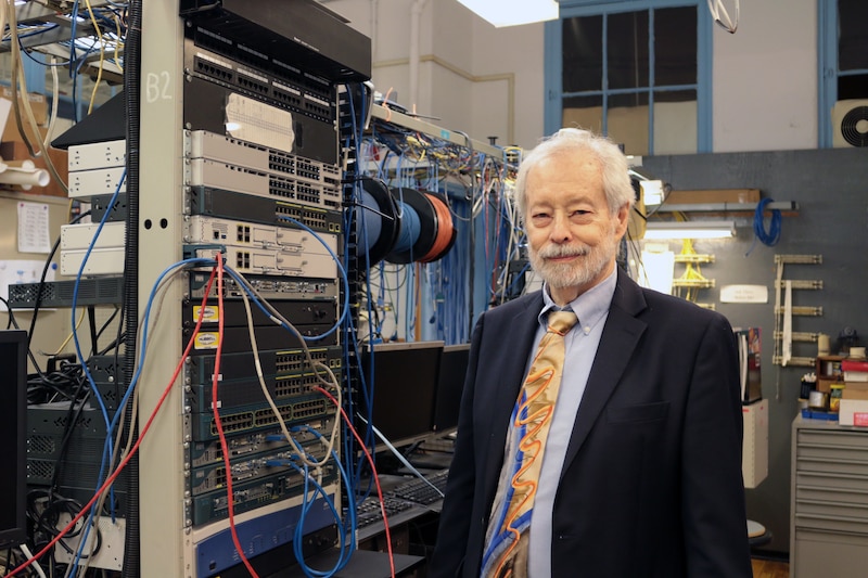 A man in a suit stands next to large computer equipment.