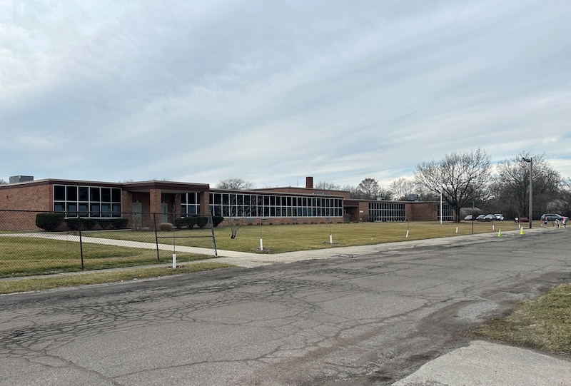 A large red brick building in the background with a large grassy lawn in the foreground.