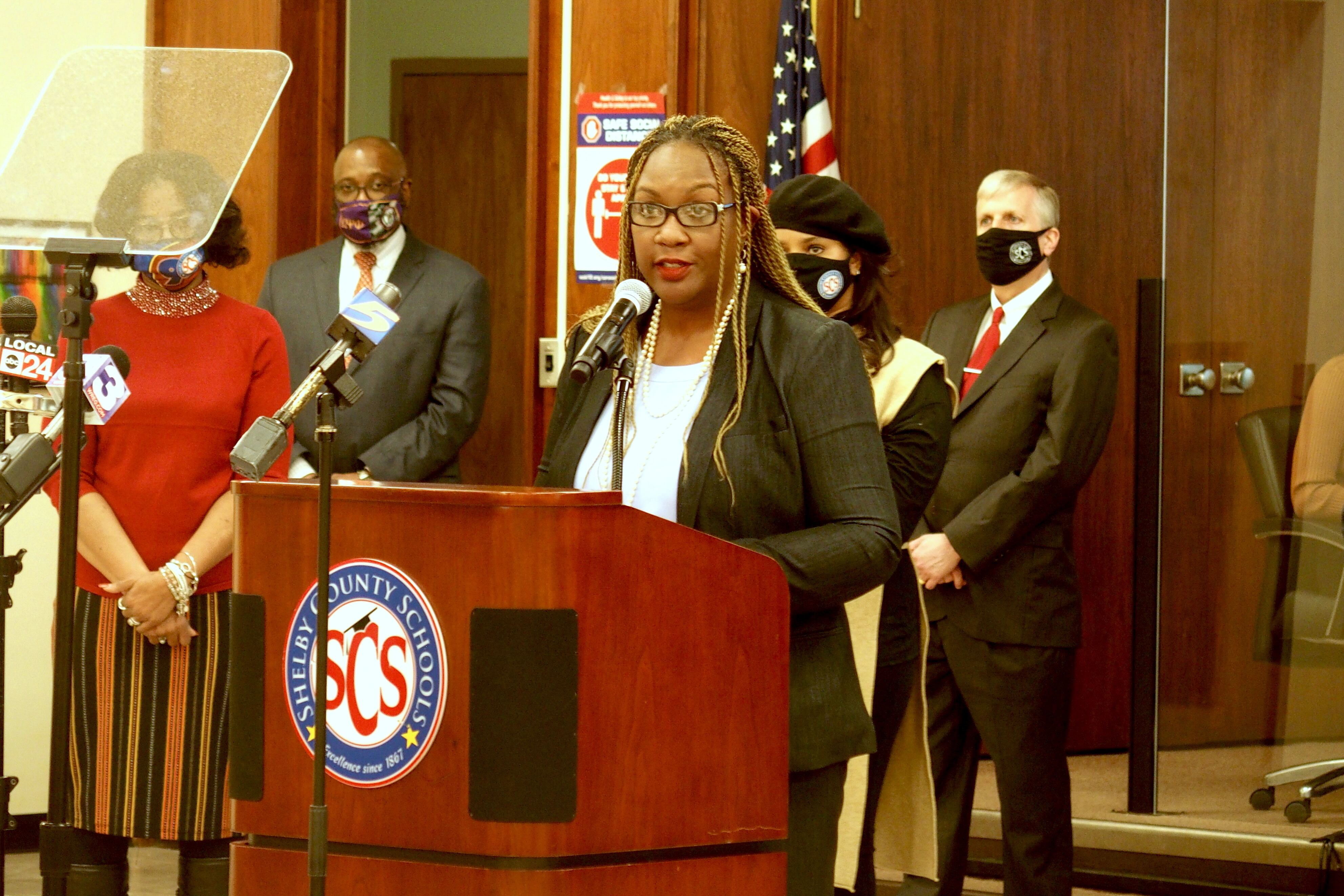A woman wearing glasses speaks into a microphone while standing at a podium in Shelby County Schools’ central office auditorium.