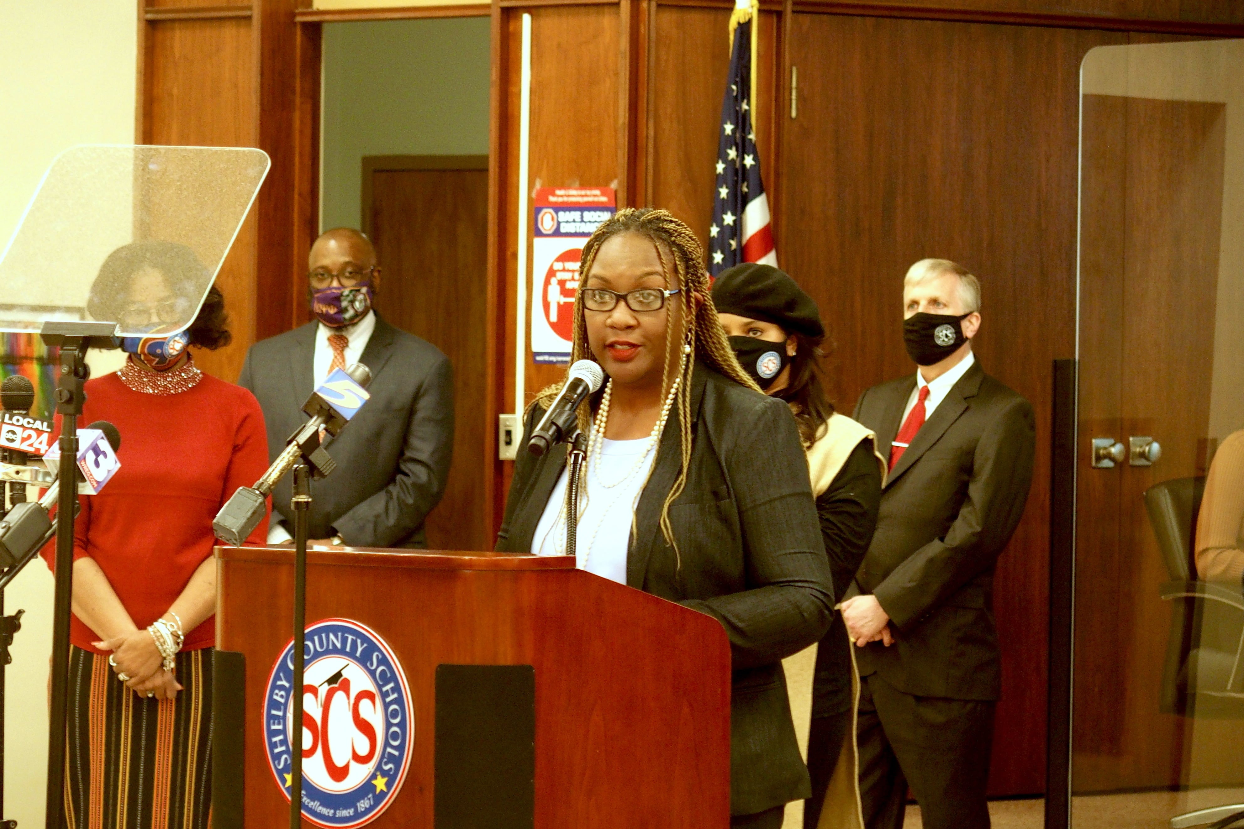 A woman wearing glasses speaks into a microphone while standing at a podium in Shelby County Schools’ central office auditorium.