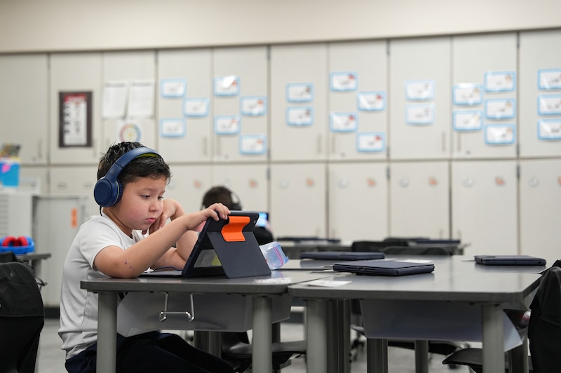 A boy sits and looks at an ipad. He's wearing headphones.
