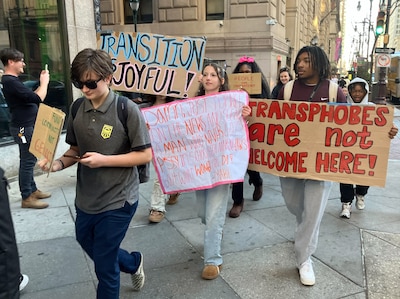 A group of students holding signs walk down the street.