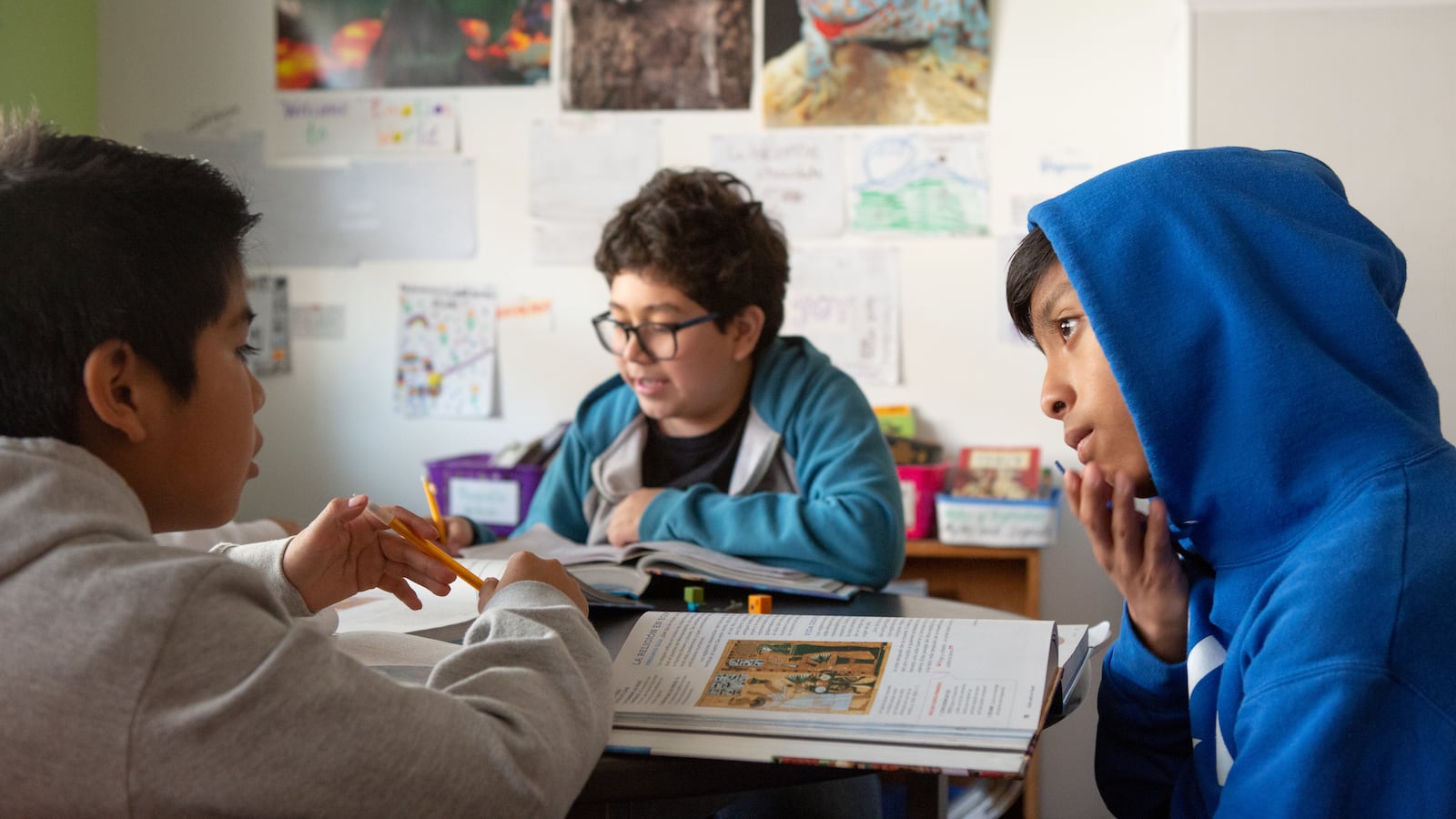 Three people sit around a table with pictures on a wall in the background