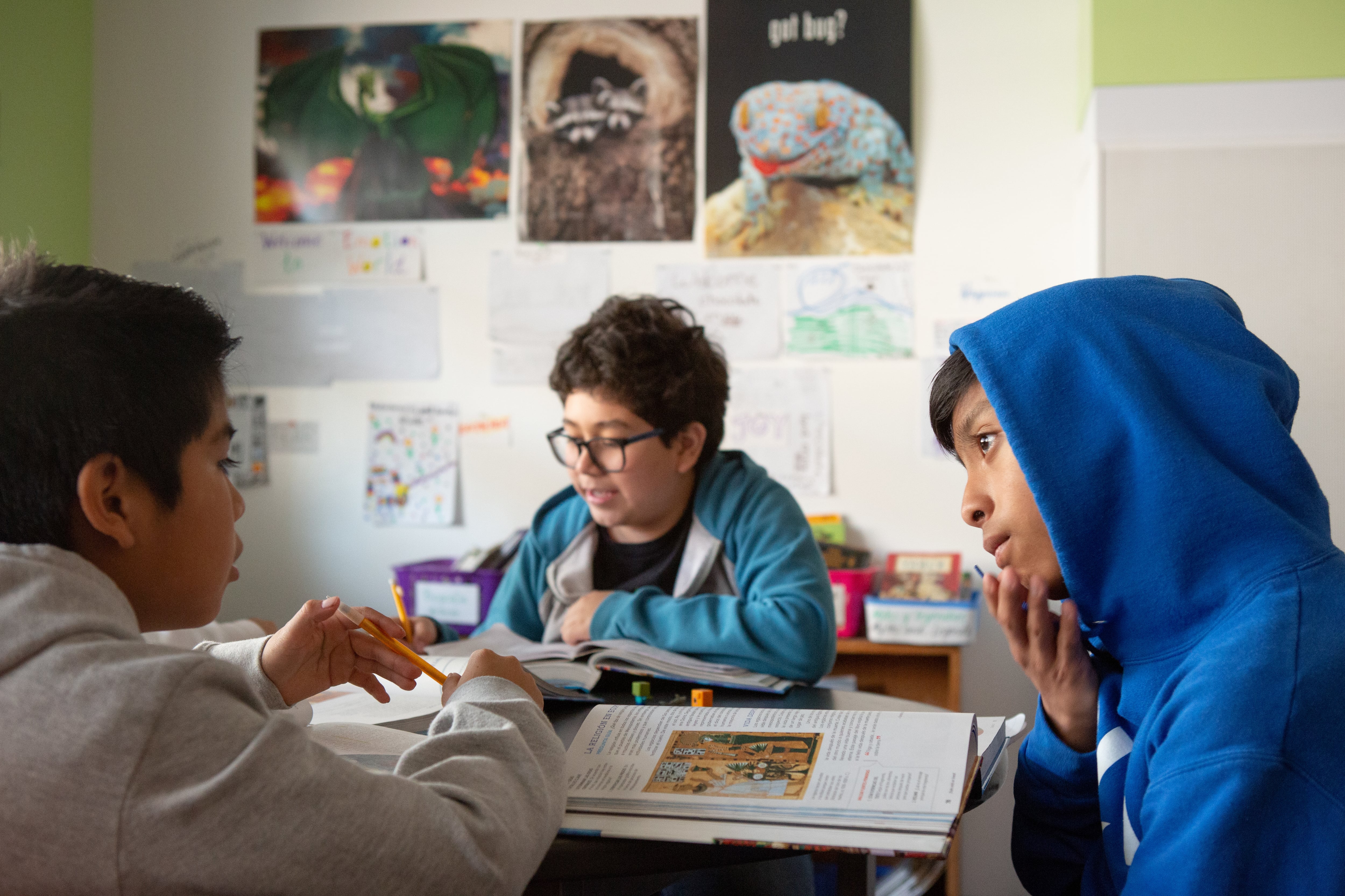 Three people sit around a table with pictures on a wall in the background