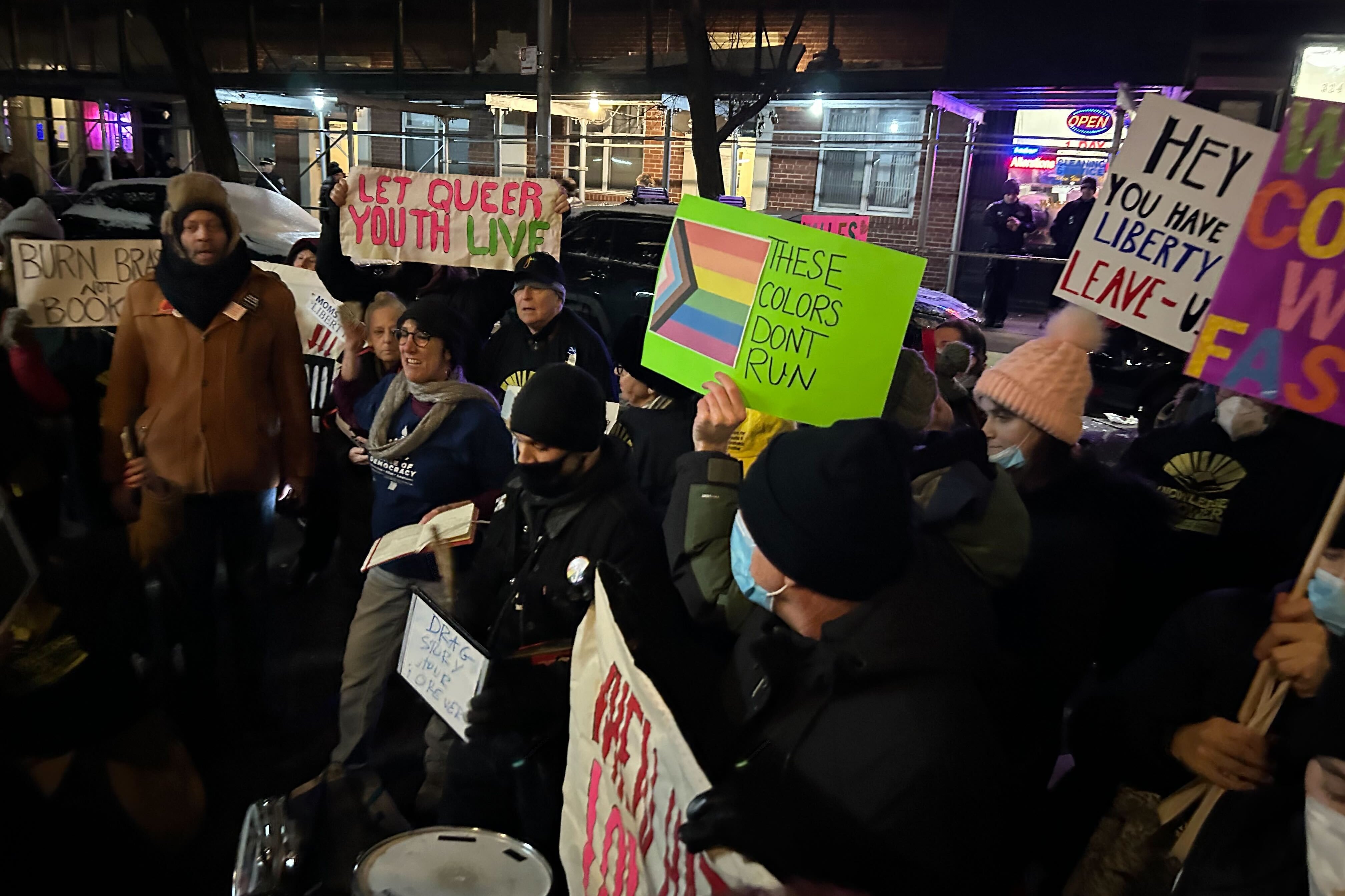 A group of protesters hold signs such as "Let queer youth live."