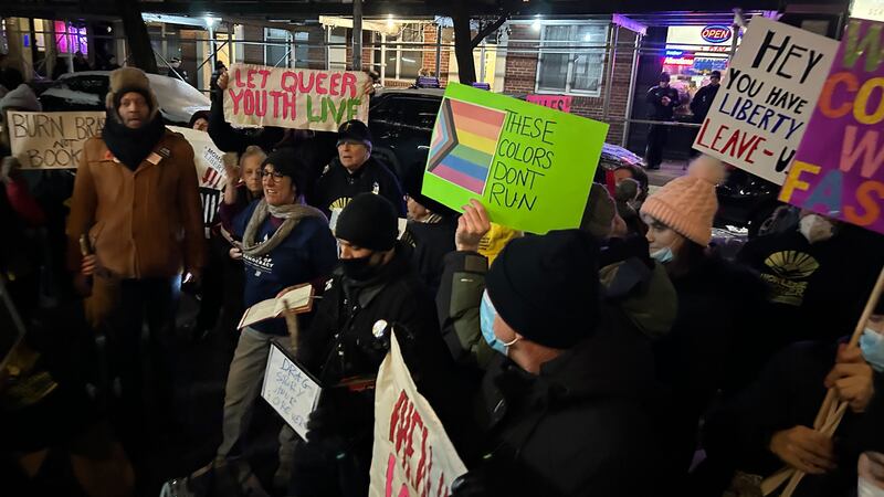 A group of protesters hold signs such as "Let queer youth live."