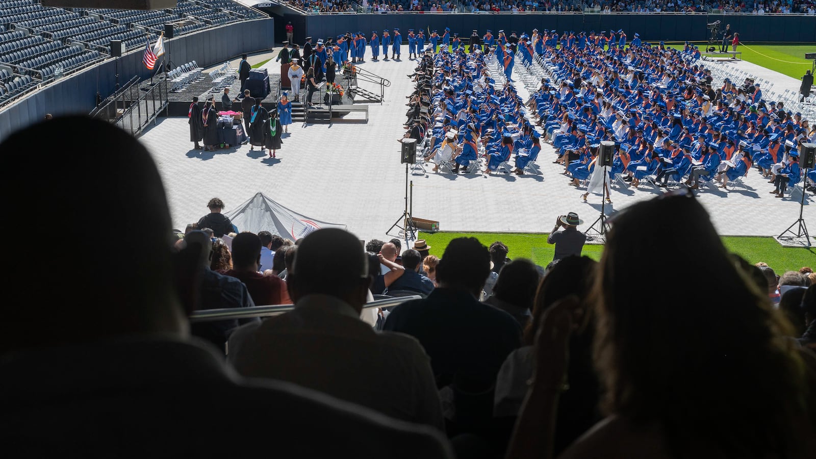 A crowd of people watch from stadium seats as their loved ones begin to walk to the stage for their diplomas.