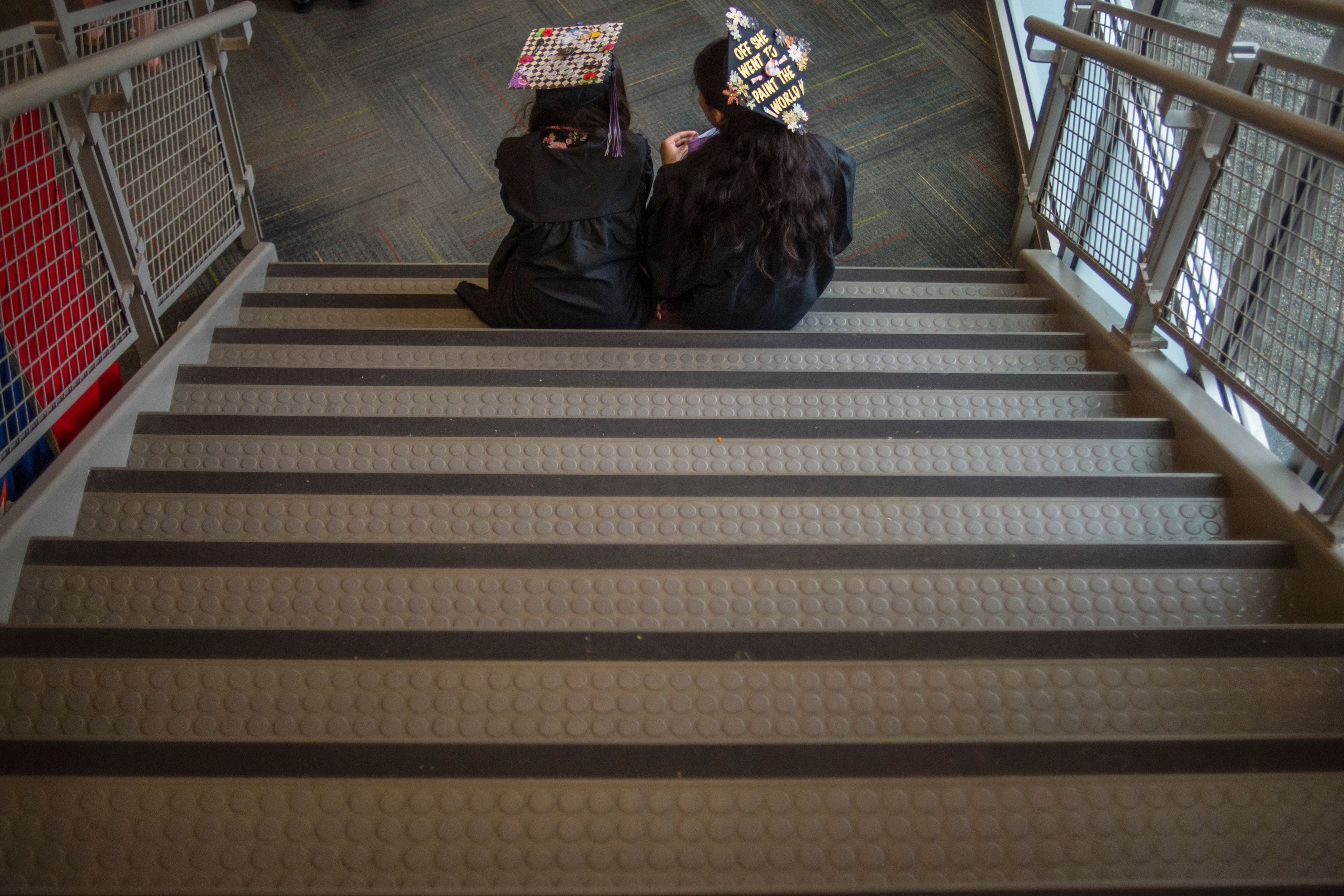 High school graduates in caps and gowns sit on a staircase.