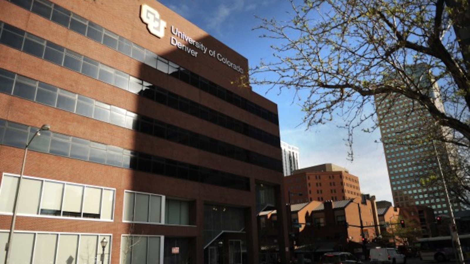 A brown building with windows at the University of Colorado Denver campus against the backdrop of other city buildings and a blue sky.