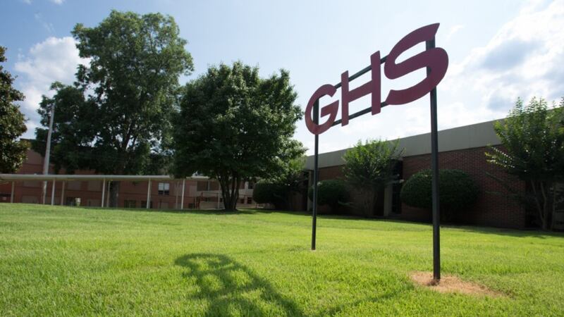 A sign that says “GHS” sits in front of a school building surrounded by a green campus.
