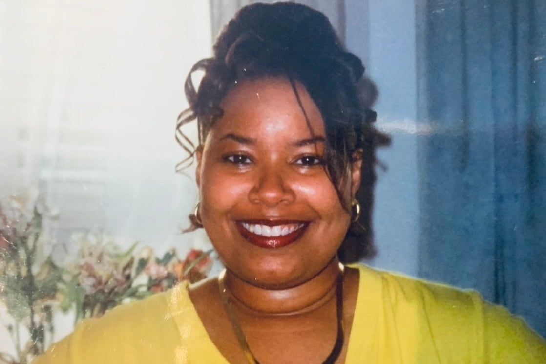 A woman with a bright yellow shirt wearing a necklace smiles and poses for a portrait.