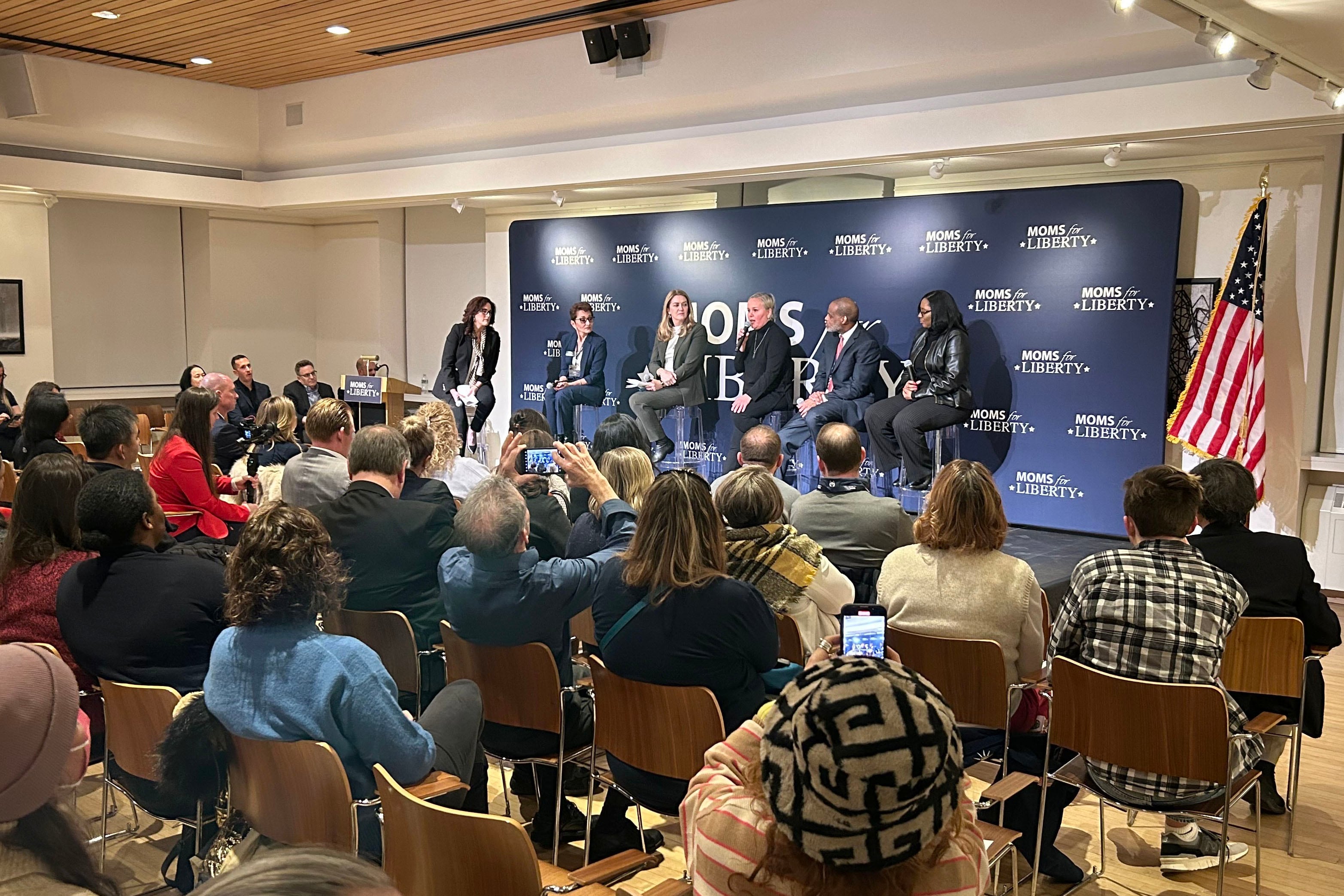 A group of adults on stage in front of a banner and a crowd of people sitting in chairs.