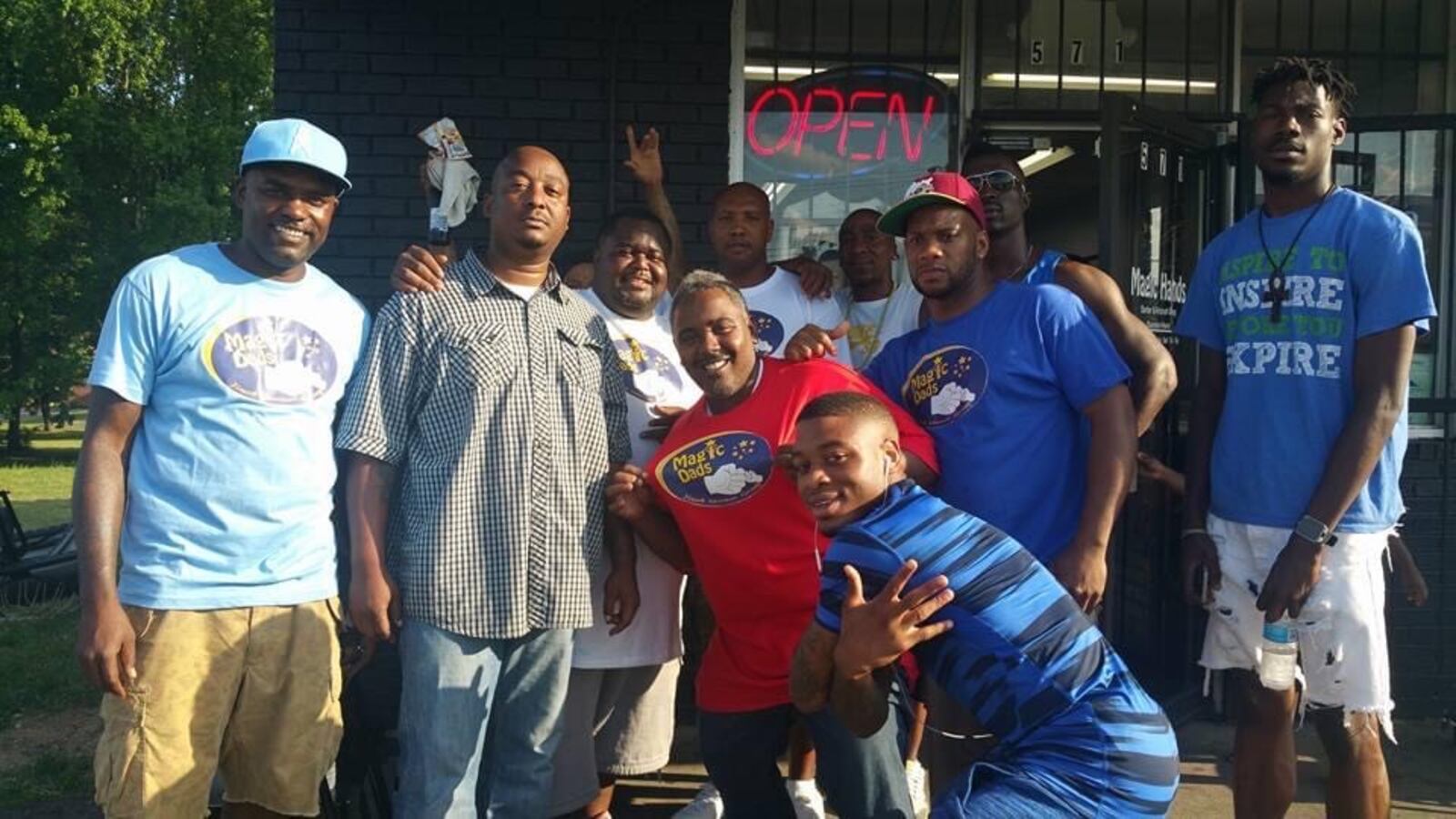 A group of men with Magic Dads mentoring group gather together cheerfully on the sidewalk for a photo.