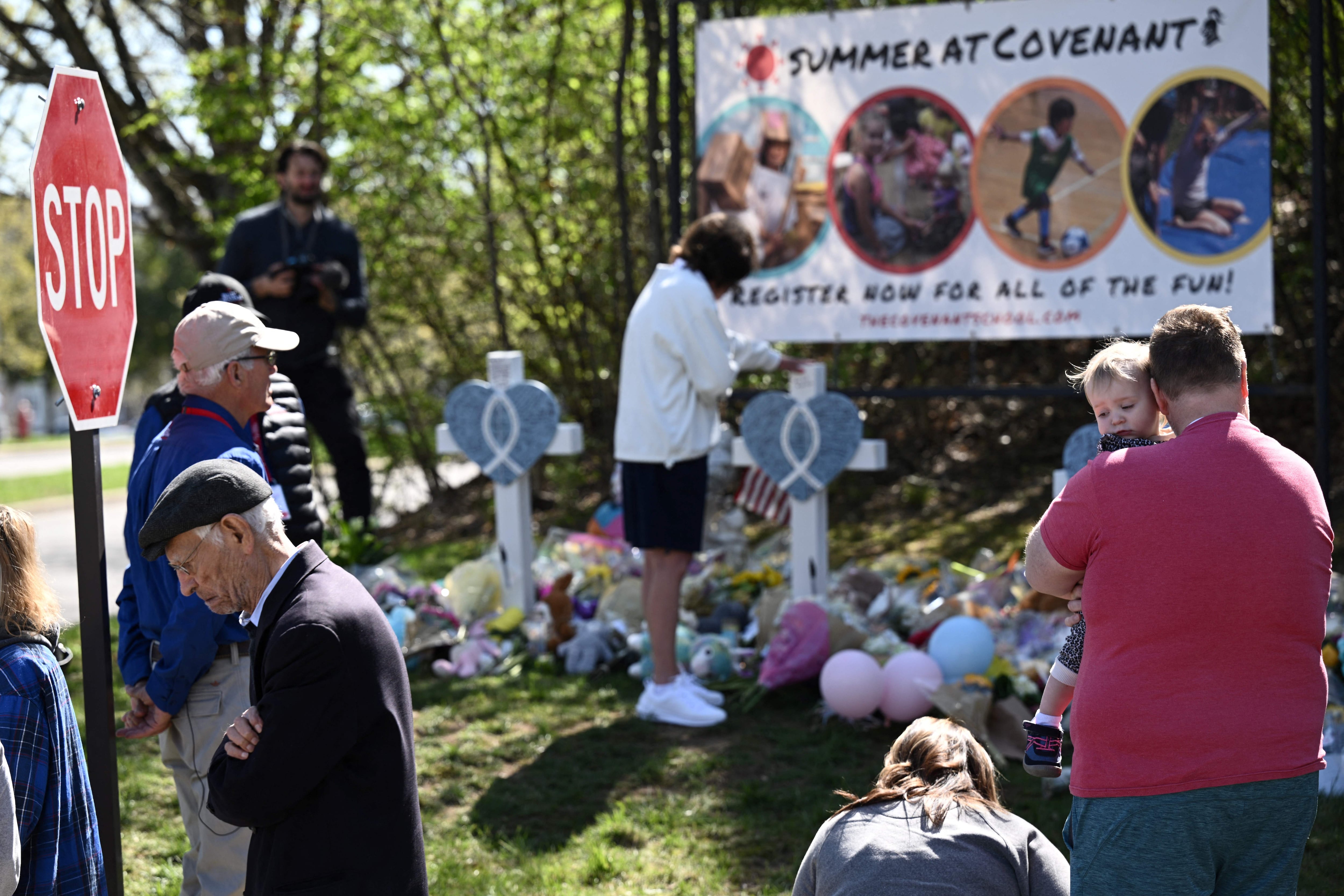 People stand near a makeshift roadside memorial. One man holds a child.