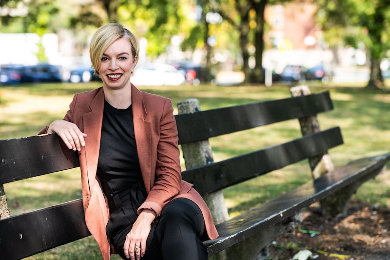 A woman with a brown jacket sits on a bench.