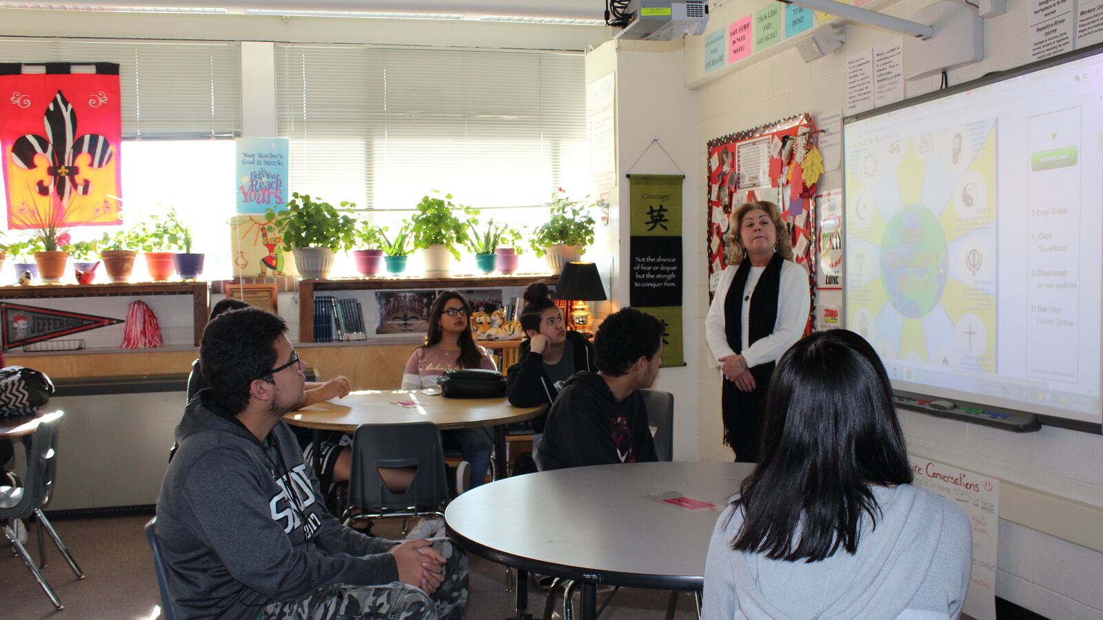 An adult teacher stands up at the front of the class while older adults sit at tables in a classroom.