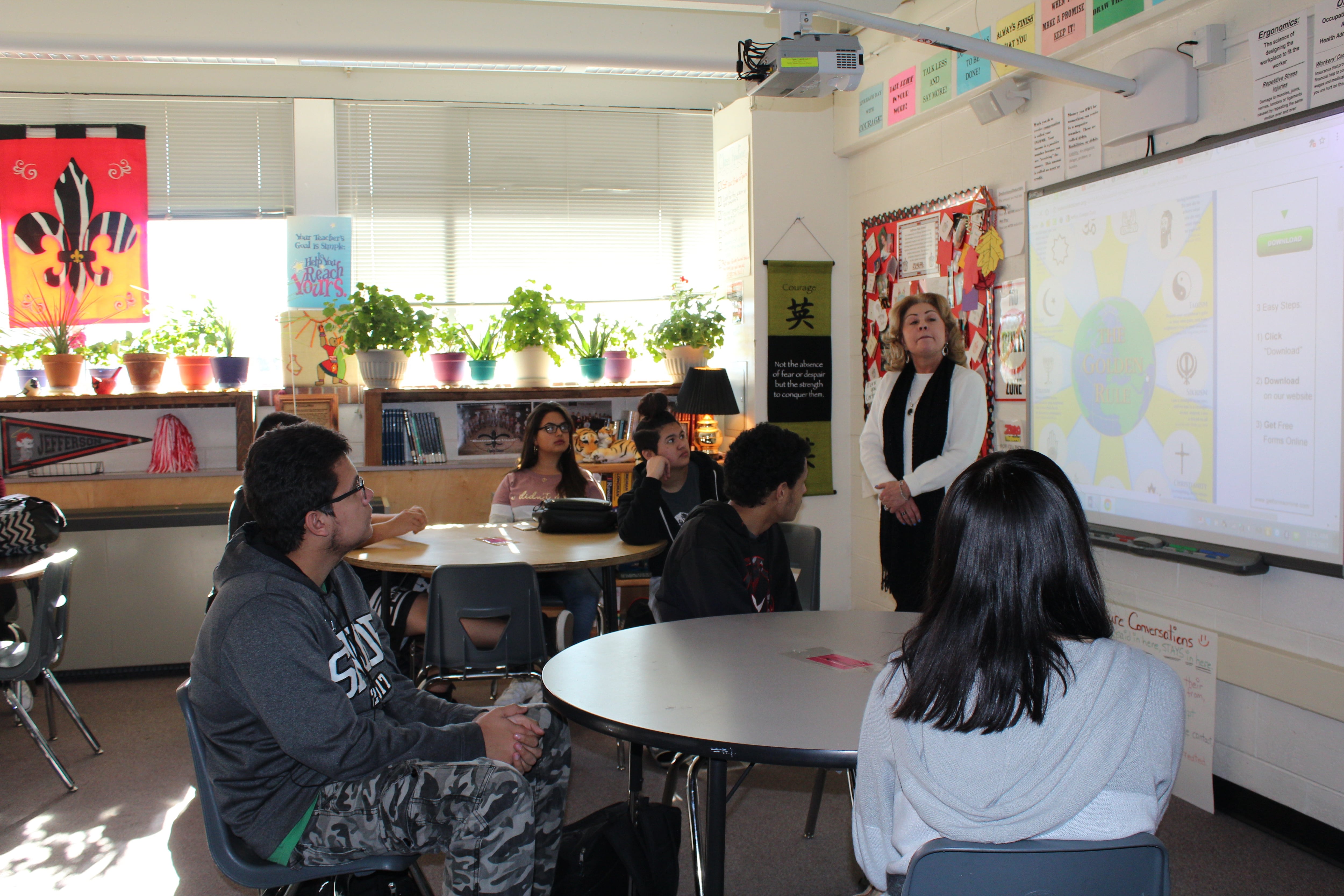 An adult teacher stands up at the front of the class while older adults sit at tables in a classroom.