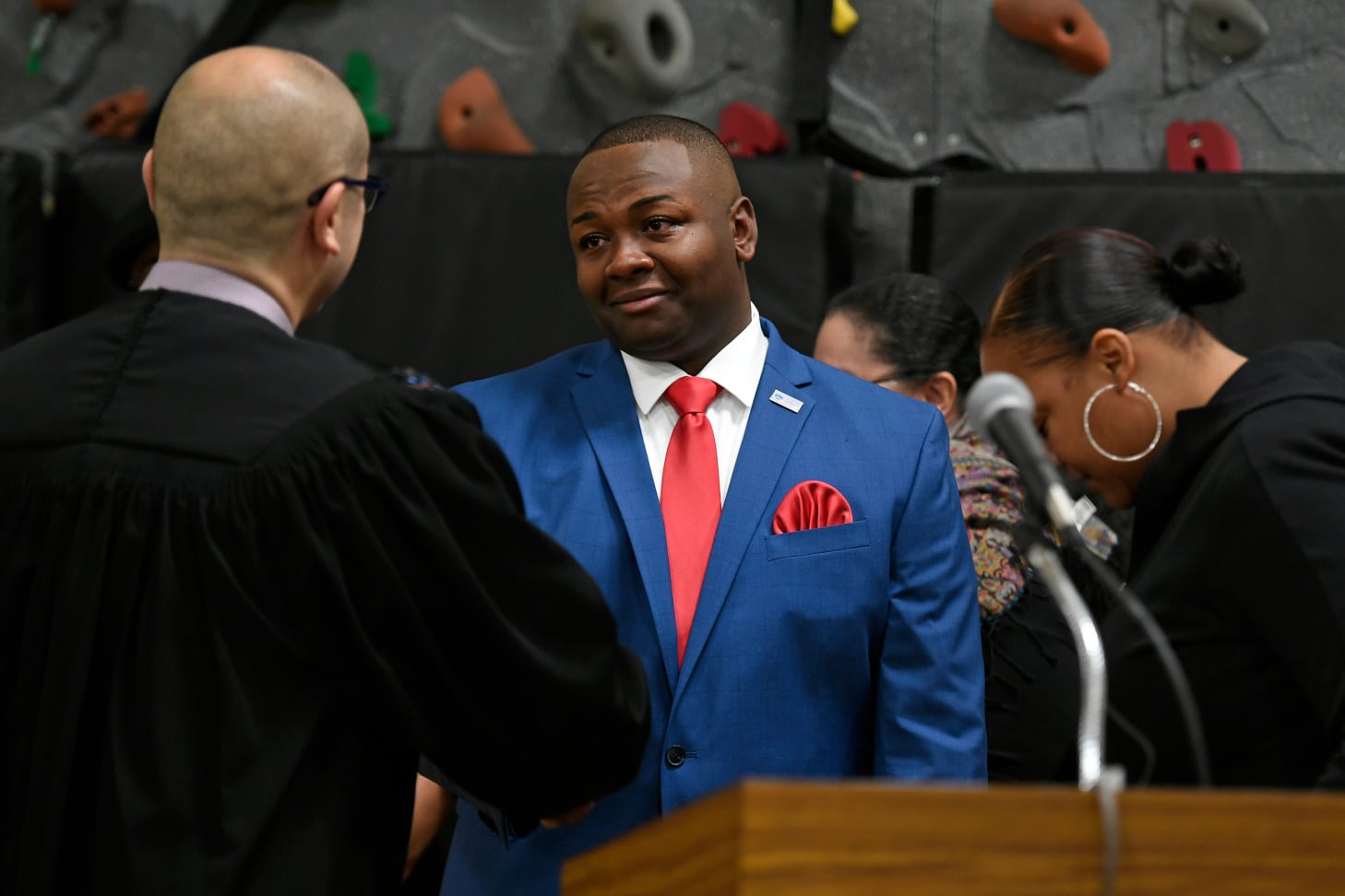 Auon’tai Anderson, wearing a blue suit with a red tie, shakes hands with a judge behind a podium after being sworn in.