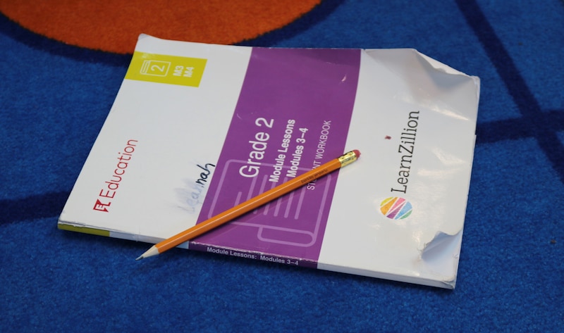 A white and purple grade 2 workbook and a pencil sit on a colorful rug.
