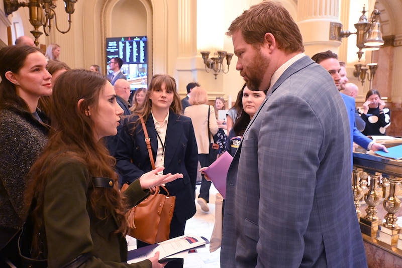 A man in a gray jacket talks to a woman in a brown jacket.