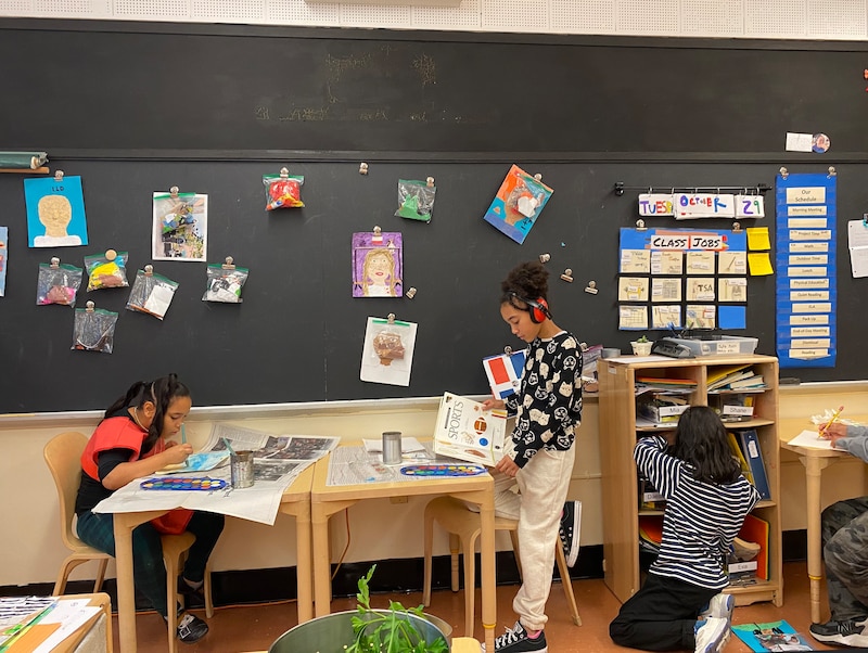 Two female students work at tables in front of a board in a classroom.