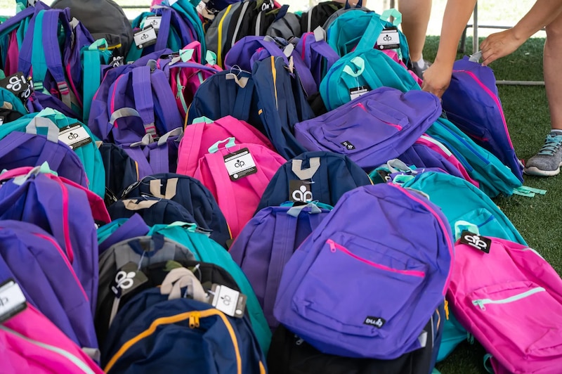 A pile of purple, pink, and blue backpacks at a back-to-school giveaway.