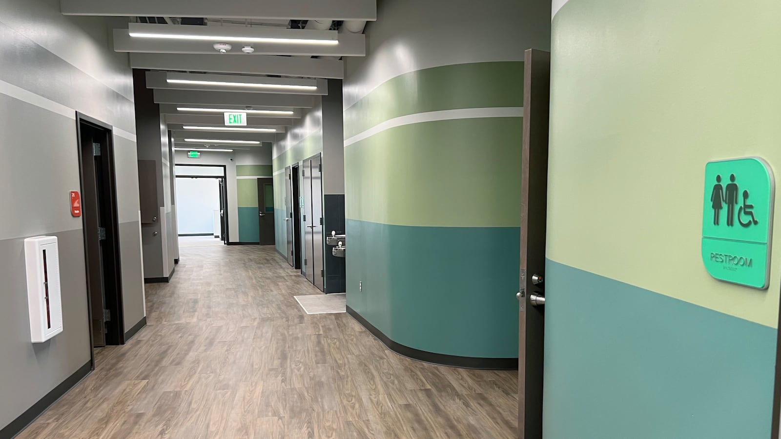 A hallway with grey and different shades of green on the wall with a wooden floor.