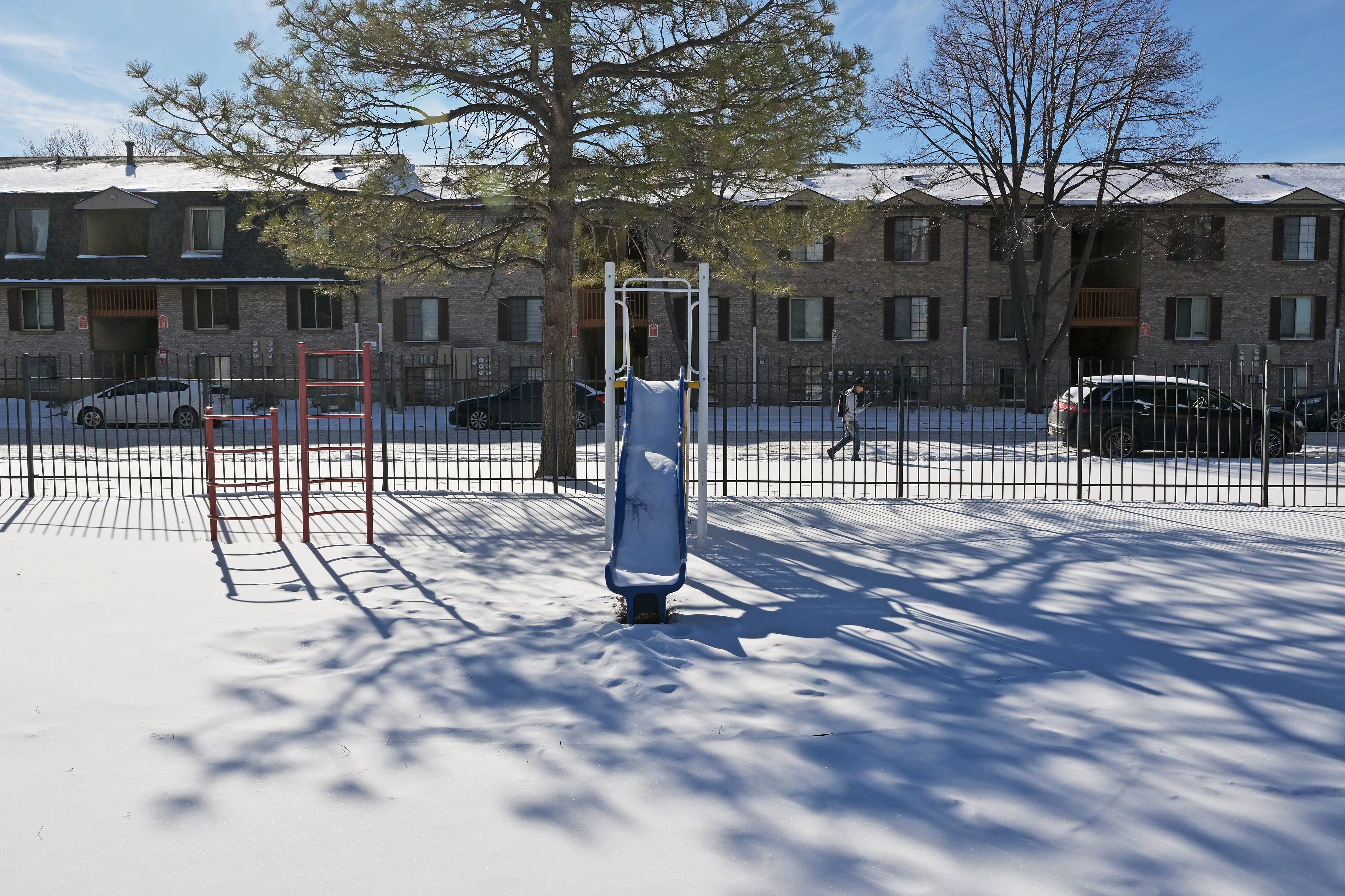 A snow covered playground in front of a housing complex outside on a sunny day.
