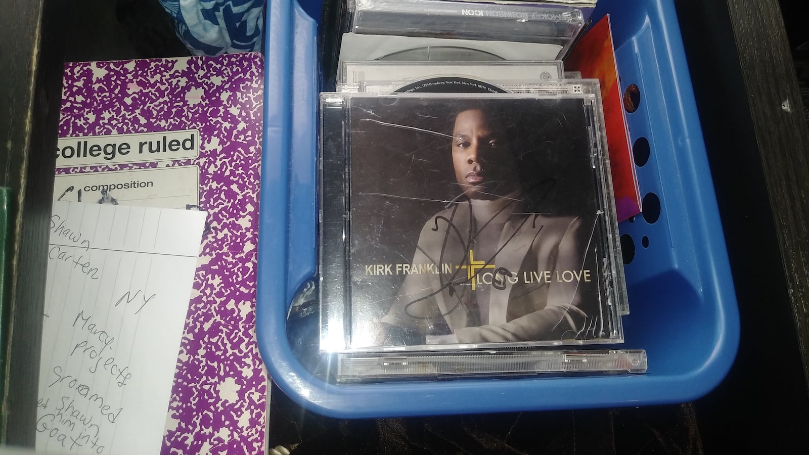 A blue plastic container filled with a stack of CDs, a Kirk Franklin CD at the top of the pile.