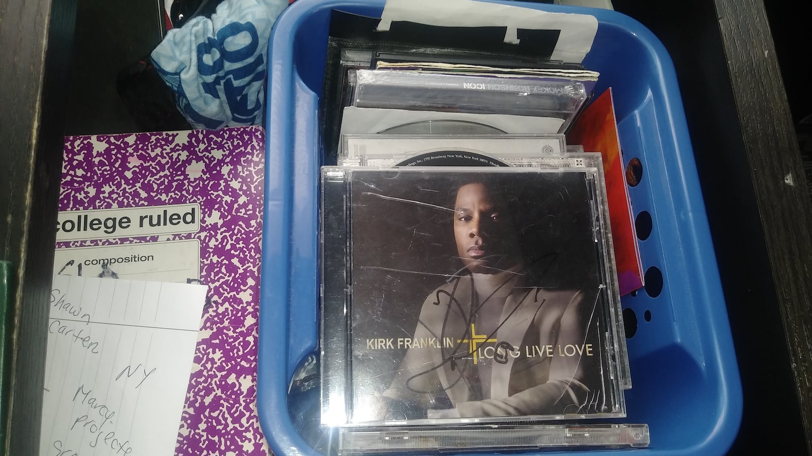 A blue plastic container filled with a stack of CDs, a Kirk Franklin CD at the top of the pile.