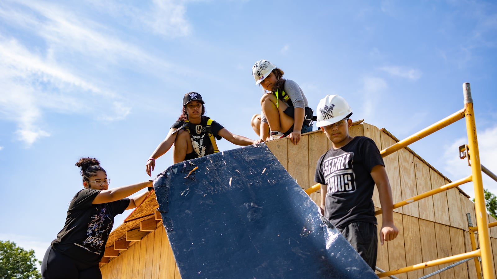 Four students work together on constructing the roof of a shed.