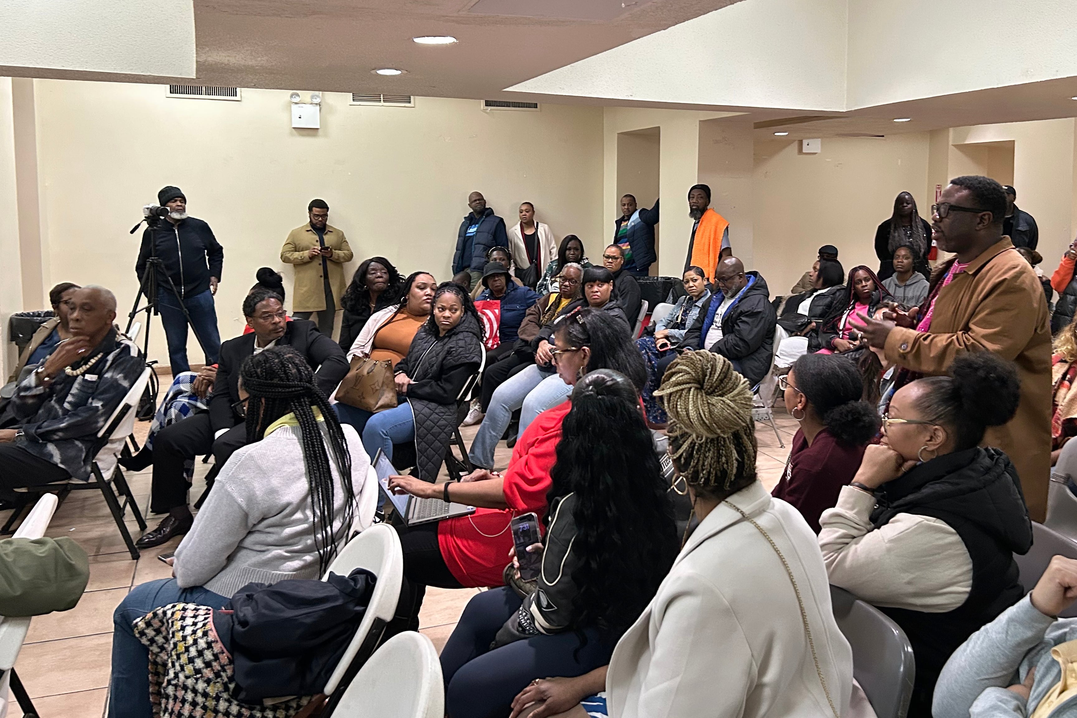 A large group of people sit in chairs during a community meeting.