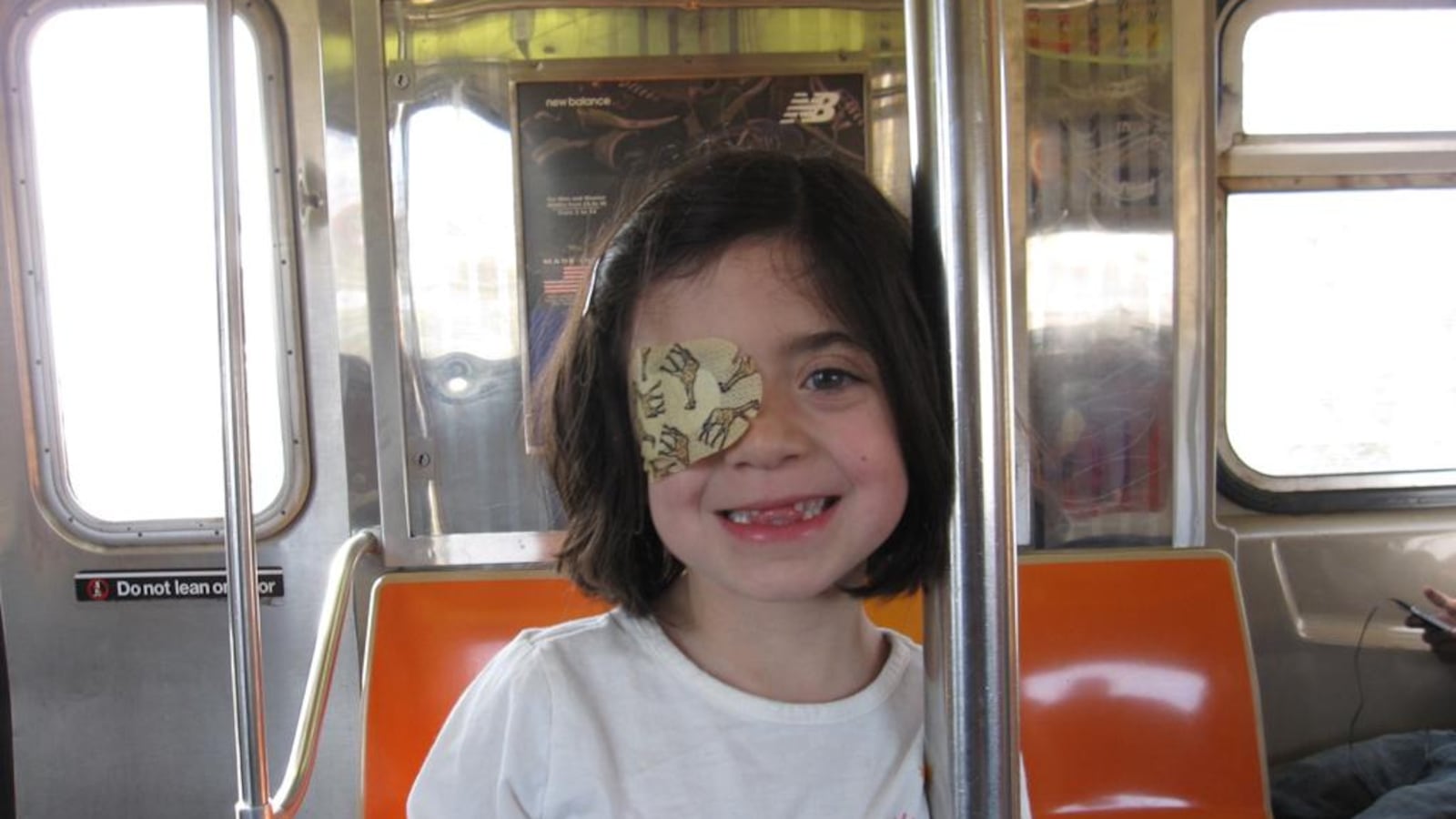 A photo of a little girl on the New York City subway. She wears a patch over her right eye. 