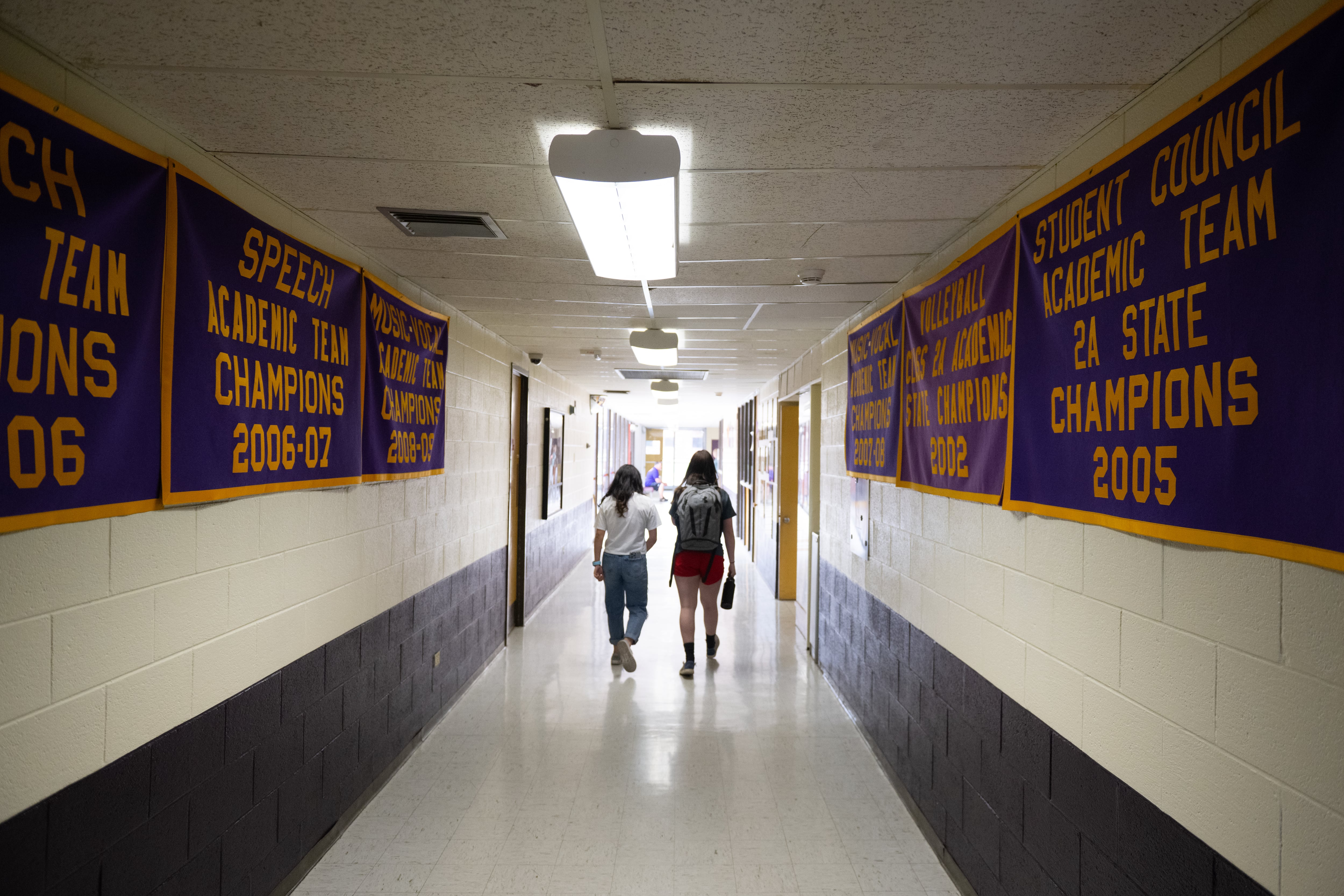Two people walk down a school hallway.