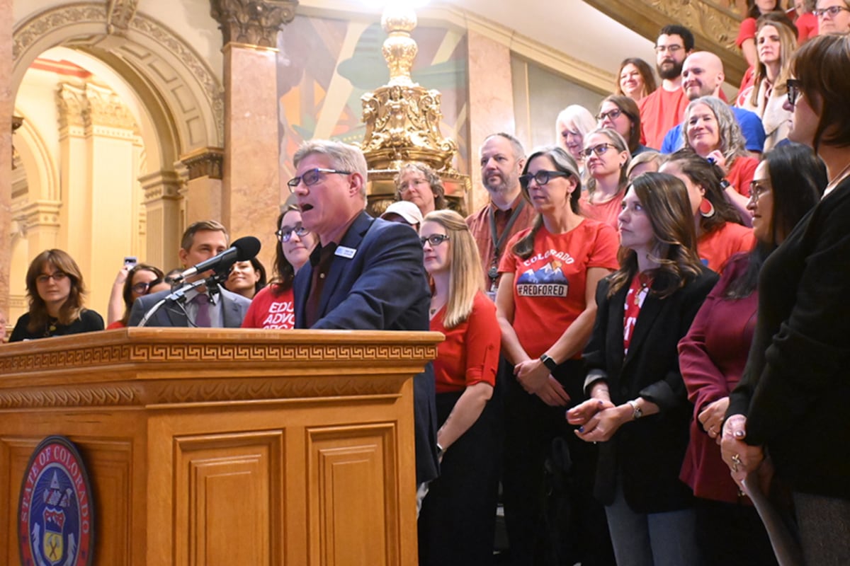 A man speaks at a poium surrounded by others.