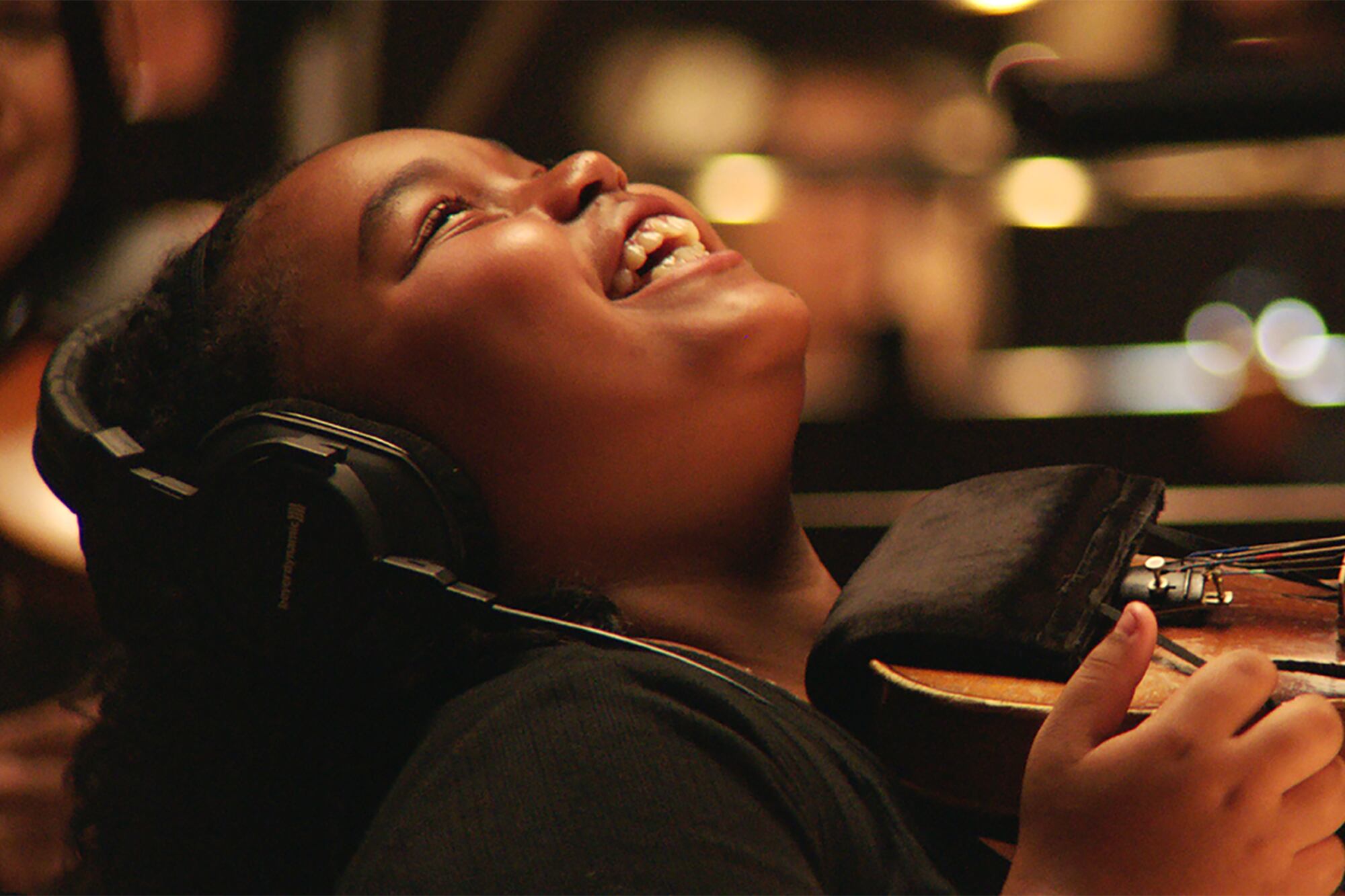 A young girl tilts her head back while she laughs and is holding a violin.