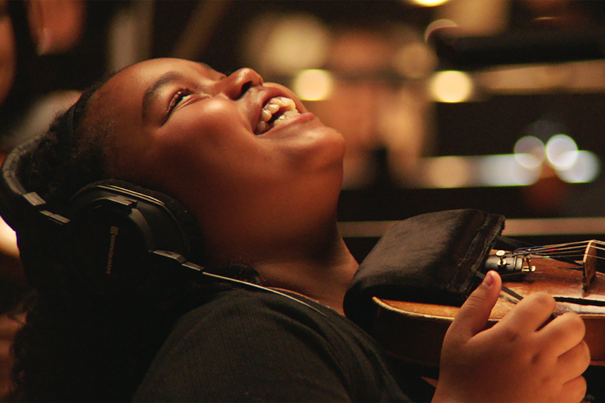 A young girl tilts her head back while she laughs and is holding a violin.